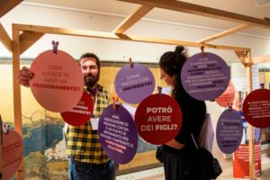 Ragazzi che leggono domande critiche (es: potrò avere figli?) in baloon appesi in un allestimento a #GiovanioltrelaSM 2022 il cui scopo è rassicurare a prire un dialogo