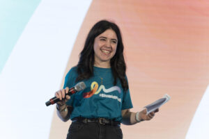 Ragazza sorridente parla sul palco ai talk di #GiovanioltrelaSM - Tempo